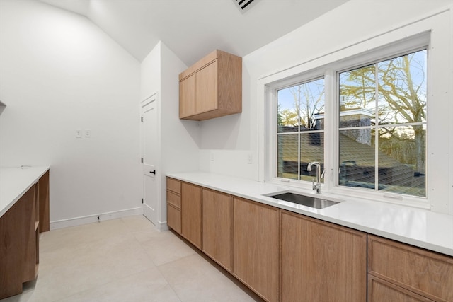 kitchen featuring brown cabinets, light countertops, vaulted ceiling, a sink, and baseboards