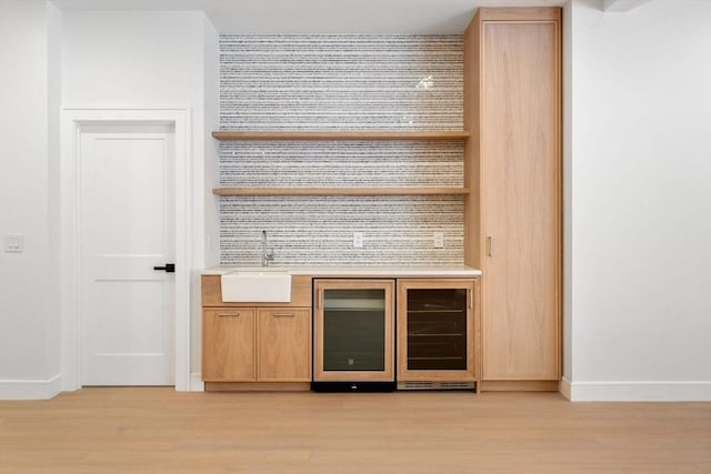 bar with beverage cooler, indoor wet bar, a sink, and light wood-style flooring