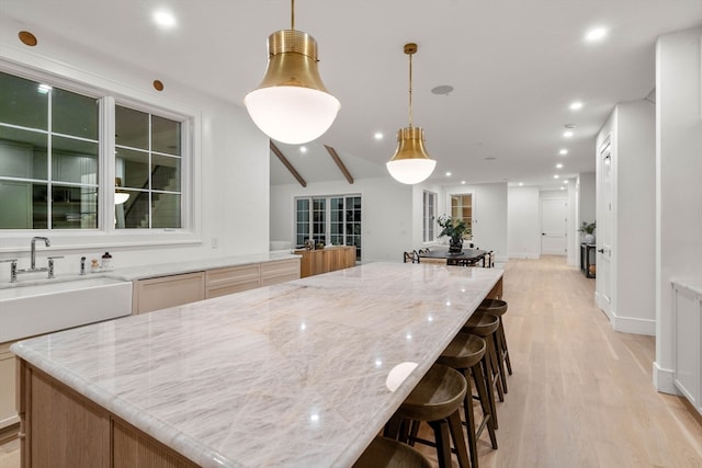 kitchen featuring light wood finished floors, a large island, light stone countertops, pendant lighting, and a sink