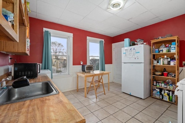 kitchen featuring light tile patterned floors, a paneled ceiling, sink, and white fridge