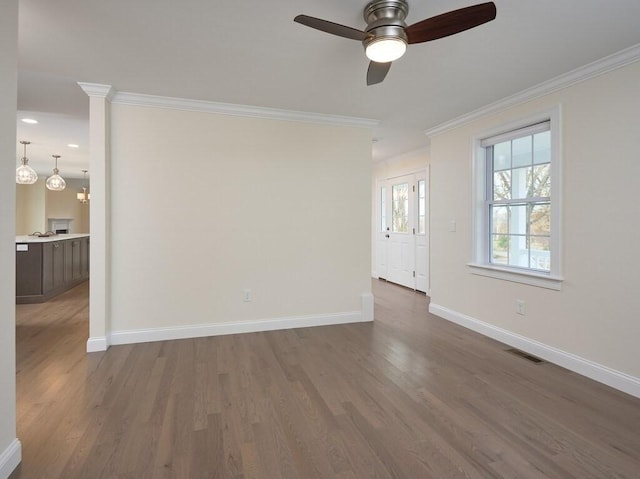 empty room featuring baseboards, visible vents, dark wood finished floors, a ceiling fan, and ornamental molding