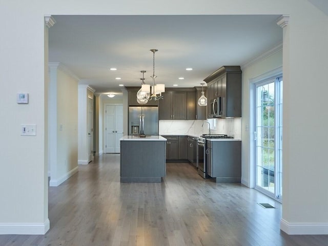 kitchen featuring a kitchen island, appliances with stainless steel finishes, ornamental molding, hanging light fixtures, and light countertops