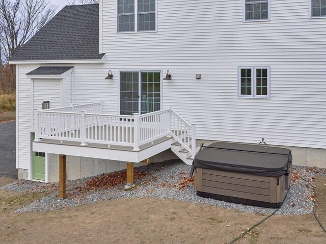 exterior space with roof with shingles, a hot tub, and a wooden deck