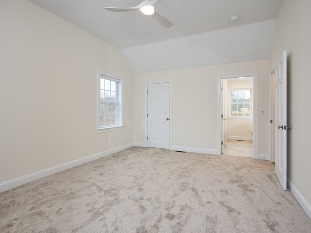 unfurnished bedroom with light carpet, connected bathroom, vaulted ceiling, ceiling fan, and baseboards