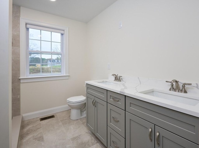 bathroom with toilet, double vanity, a sink, and visible vents