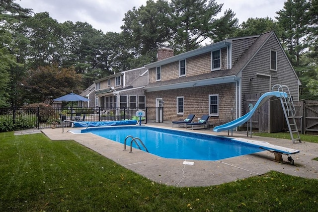 view of swimming pool with a patio area, a diving board, a lawn, and a water slide