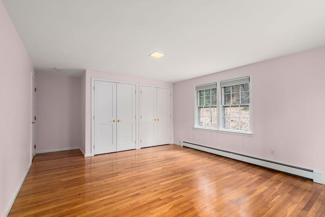unfurnished bedroom featuring light wood-type flooring, multiple closets, baseboards, and baseboard heating