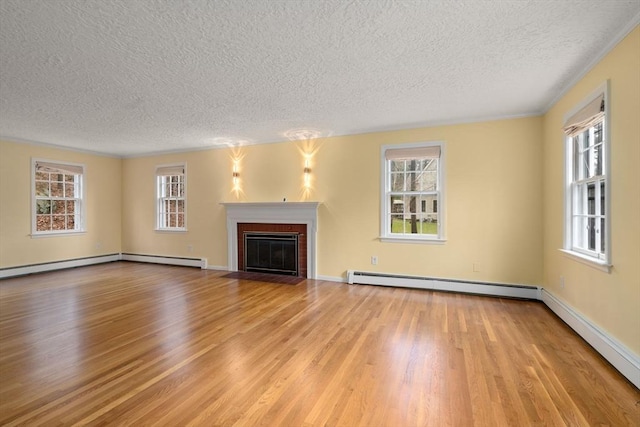 unfurnished living room with baseboard heating, a textured ceiling, a healthy amount of sunlight, and wood finished floors