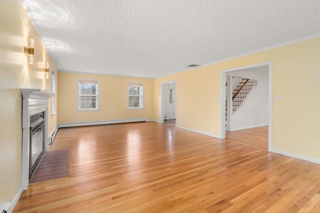 unfurnished living room with a textured ceiling, a baseboard radiator, light wood finished floors, a glass covered fireplace, and stairs