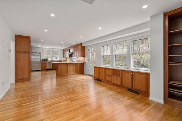 kitchen with appliances with stainless steel finishes, brown cabinets, light wood-type flooring, a peninsula, and recessed lighting