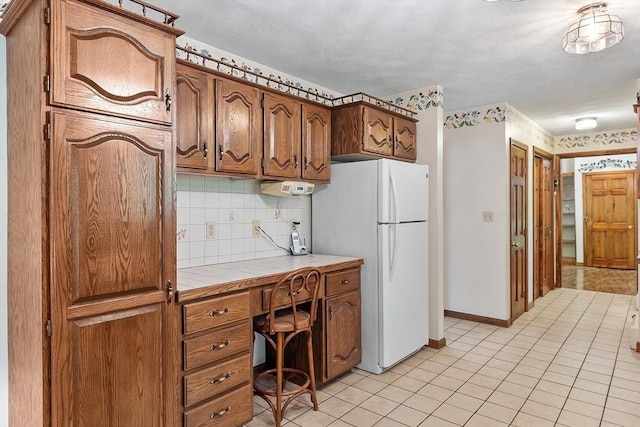 4 Clarke Rd, Littleton, MA 01460 - kitchen with freestanding refrigerator, tile counters, brown cabinets, decorative backsplash, and a desk