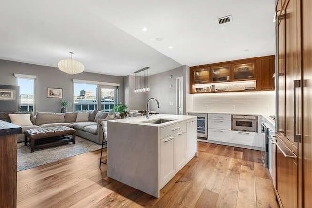 kitchen featuring visible vents, open floor plan, an island with sink, light wood-style flooring, and a sink