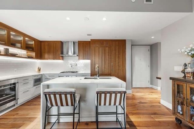 kitchen with light wood finished floors, beverage cooler, light countertops, wall chimney exhaust hood, and a sink