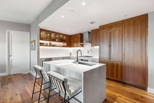 kitchen with light countertops, wall chimney range hood, light wood-style flooring, and a sink