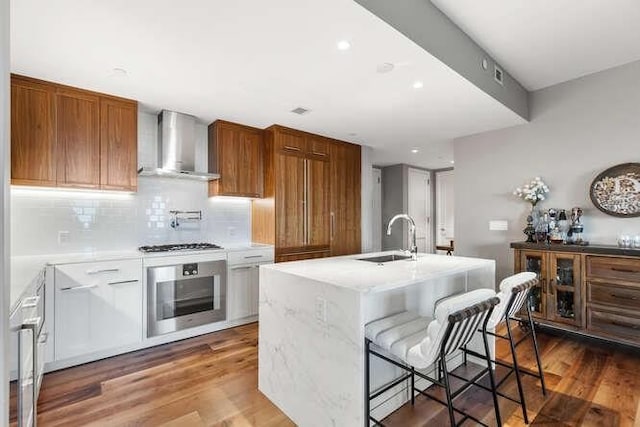 kitchen with oven, a sink, backsplash, wood finished floors, and wall chimney exhaust hood