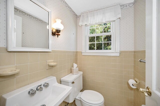 146 Elm St, Andover, MA 01810 - bathroom with wallpapered walls, toilet, tile walls, wainscoting, and a sink