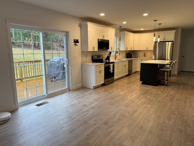 kitchen with pendant lighting, sink, appliances with stainless steel finishes, a kitchen island, and white cabinetry