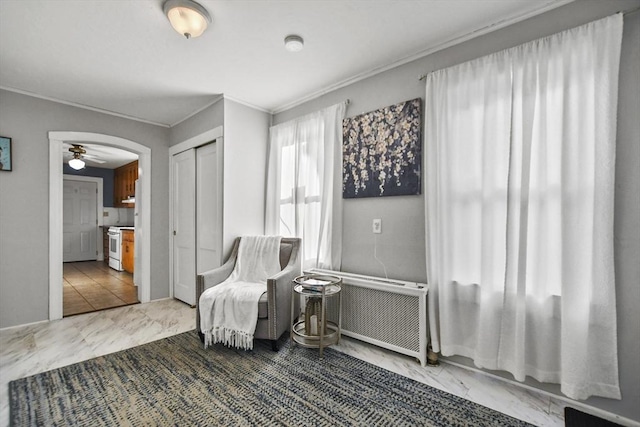 living area with ceiling fan, radiator heating unit, and ornamental molding