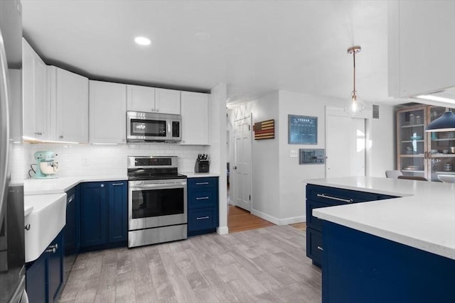 kitchen featuring appliances with stainless steel finishes, light wood-type flooring, blue cabinetry, pendant lighting, and white cabinetry