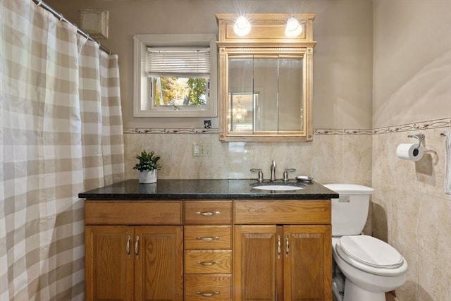 full bath with toilet, vanity, wainscoting, and tile walls