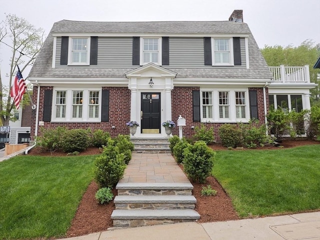 dutch colonial with brick siding, a front lawn, and a chimney