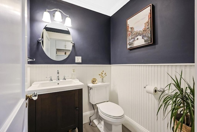 bathroom featuring a wainscoted wall, toilet, vanity, and crown molding