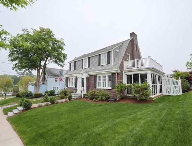 view of front of house with a balcony, brick siding, a chimney, and a front yard