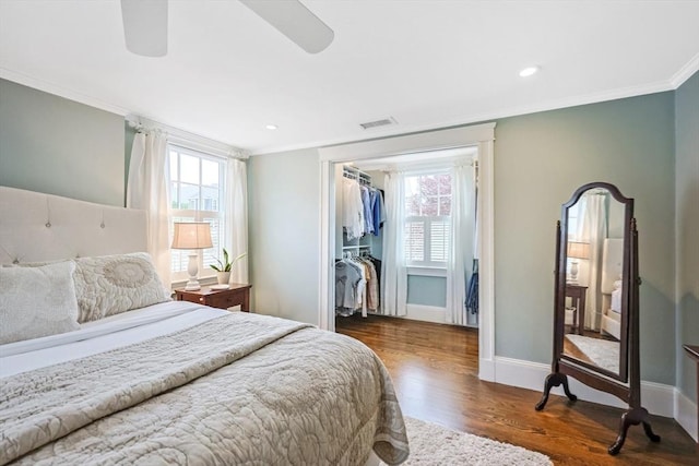 bedroom featuring crown molding, wood finished floors, multiple windows, baseboards, and a walk in closet