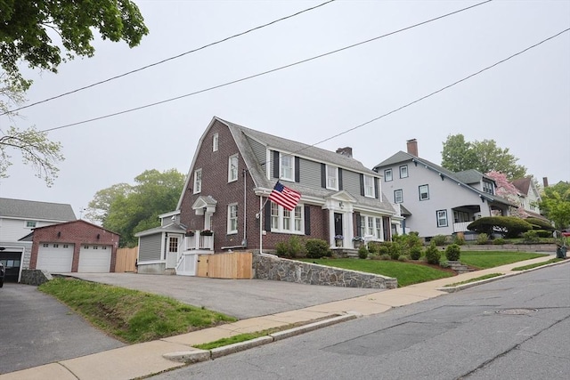 colonial inspired home featuring a residential view, brick siding, a gambrel roof, a detached garage, and an outdoor structure