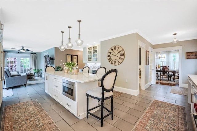 kitchen featuring a kitchen breakfast bar, white cabinets, ornamental molding, light stone countertops, and decorative light fixtures