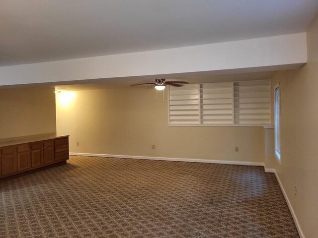 basement featuring baseboards, ceiling fan, and dark carpet