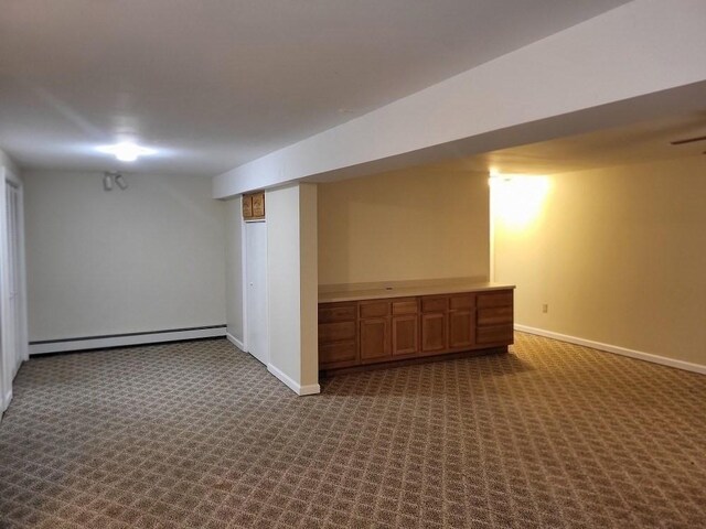 finished basement featuring baseboards, baseboard heating, and dark colored carpet