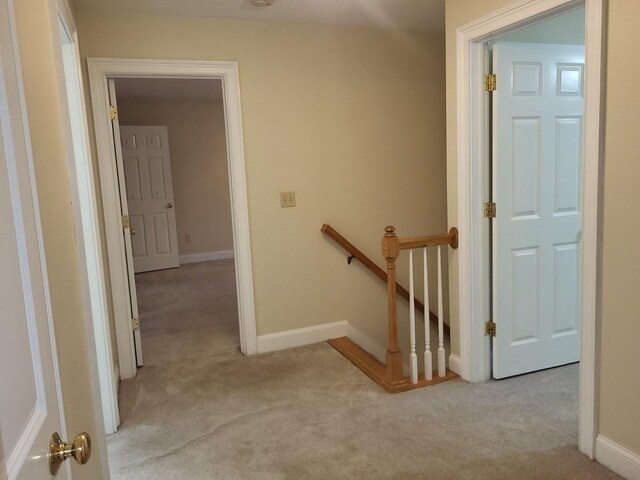 corridor with light colored carpet, an upstairs landing, and baseboards