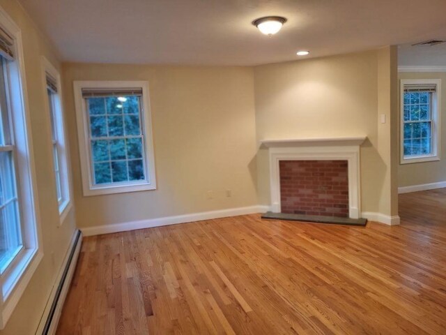 unfurnished living room with baseboards, visible vents, wood finished floors, and a baseboard heating unit