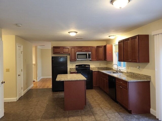 kitchen with baseboards, light stone countertops, a kitchen island, a sink, and black appliances
