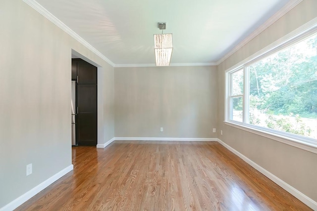 spare room with crown molding, a notable chandelier, and light wood-type flooring