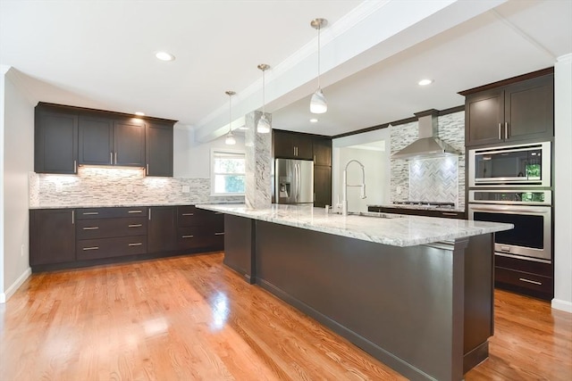 kitchen with a spacious island, sink, hanging light fixtures, stainless steel appliances, and wall chimney range hood