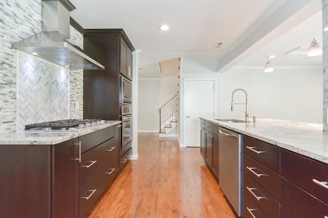 kitchen featuring sink, pendant lighting, stainless steel appliances, light stone countertops, and wall chimney range hood