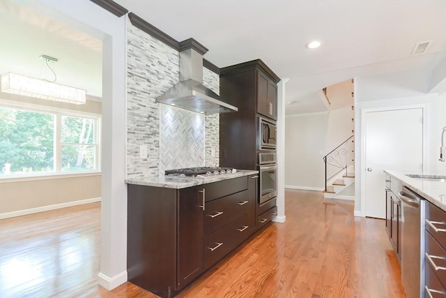 kitchen featuring wall chimney range hood, stainless steel appliances, tasteful backsplash, light stone counters, and light hardwood / wood-style floors