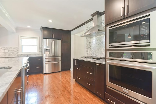 kitchen with wall chimney exhaust hood, dark brown cabinetry, stainless steel appliances, and light stone counters