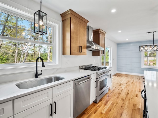 kitchen featuring white cabinets, stainless steel appliances, wall chimney range hood, and a wealth of natural light