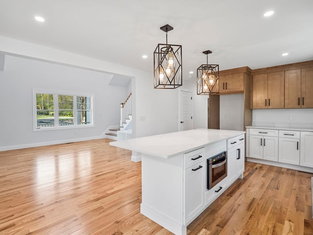 kitchen featuring light wood-type flooring, white cabinetry, hanging light fixtures, a kitchen island, and oven