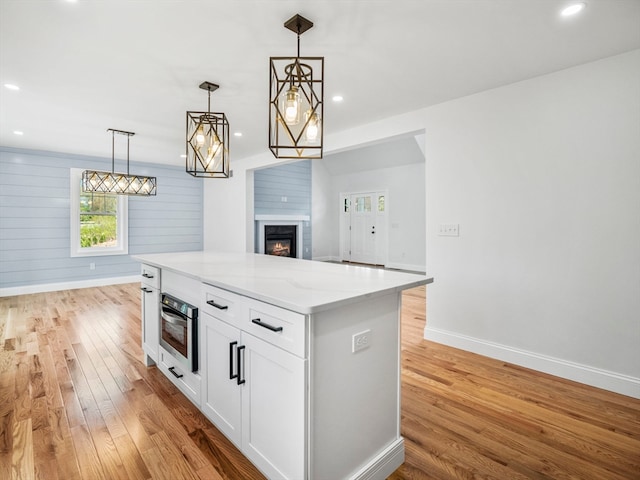 kitchen featuring white cabinets, wood walls, decorative light fixtures, stainless steel oven, and light stone countertops