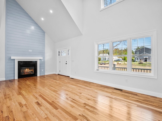 unfurnished living room featuring high vaulted ceiling, a wealth of natural light, light hardwood / wood-style floors, and a fireplace