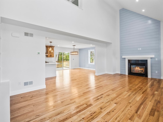 unfurnished living room with high vaulted ceiling, an inviting chandelier, light hardwood / wood-style flooring, and a fireplace