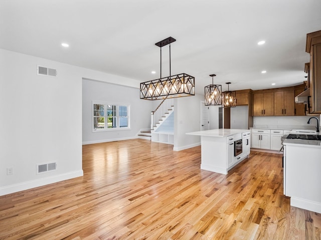 kitchen featuring light hardwood / wood-style floors, a center island, sink, white cabinets, and decorative light fixtures