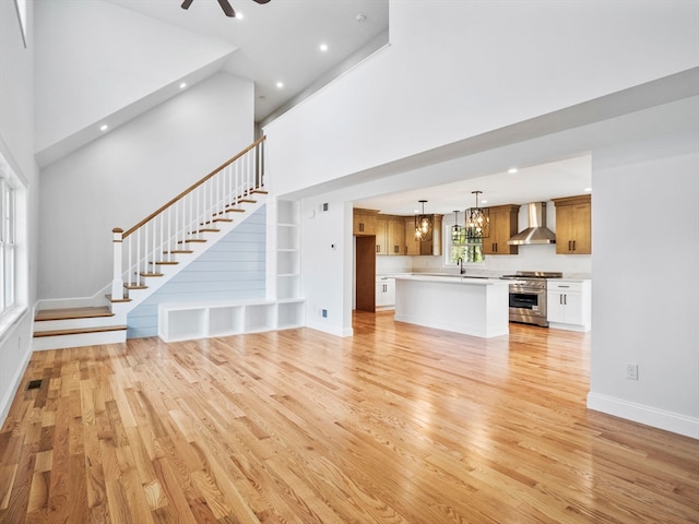 unfurnished living room with ceiling fan, light wood-type flooring, and a high ceiling