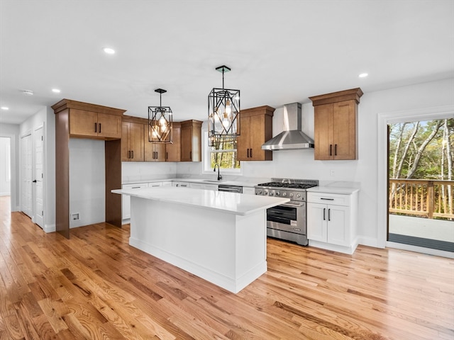 kitchen with pendant lighting, light wood-type flooring, a kitchen island, wall chimney range hood, and stainless steel appliances