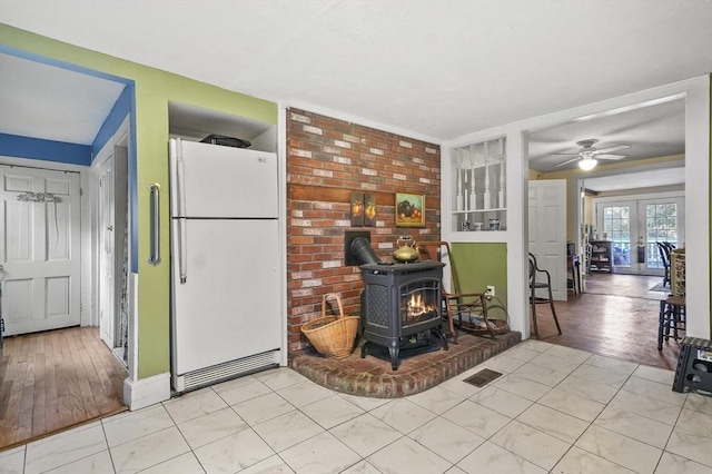 interior space with a wood stove, light tile patterned floors, a ceiling fan, and visible vents