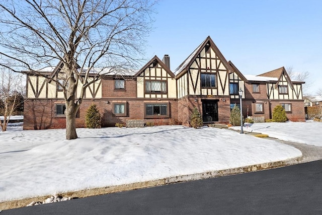 tudor-style house featuring brick siding, a chimney, and stucco siding